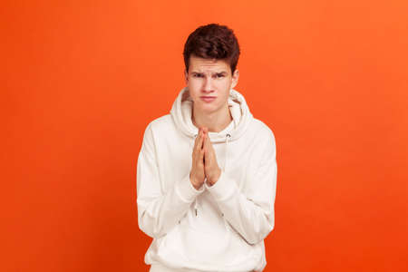 Frustrated sad teenager in casual style hoodie pressing hands together asking for help, sorry...