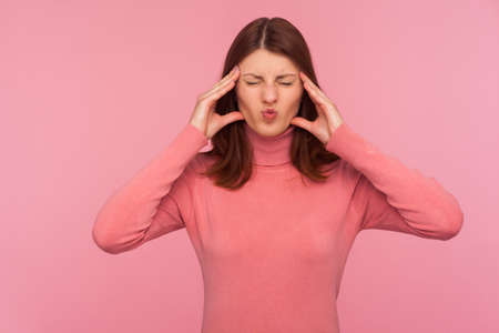 Upset brunette woman in pink sweater massaging temples with hands feeling terrible headache, risk of...