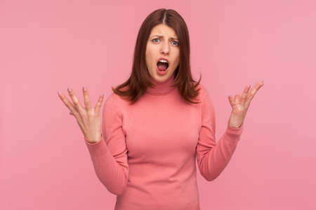 Angry unhappy brunette woman shouting raising arms up and looking at camera, blaming in treason, divorce. Indoor studio shot isolated on pink backgroundの写真素材