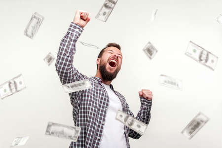 Portrait of winner man raising hands, screaming yes i did it, joyful reacting to success, victory. money rain falling from up. indoor, isolated on white backgroundの写真素材