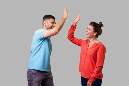 Side view portrait of excited amazed young couple in casual wear standing saying hello and giving high five, friends greeting each other, glad to meet. isolated on gray background, indoor studio shotの写真素材