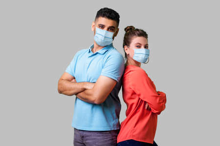 Reliable friendship. Cheerful young couple of friends with surgical medical mask standing back to...