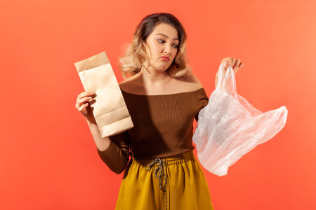 Young woman holding in hands paper and plastic bags, preferring ecological products, campaign...