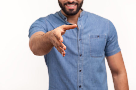 Smiling man with beard giving hand to handshake, giving hi or bye, ready to make deal, partnership. Indoor studio shot isolated on white backgroundの写真素材