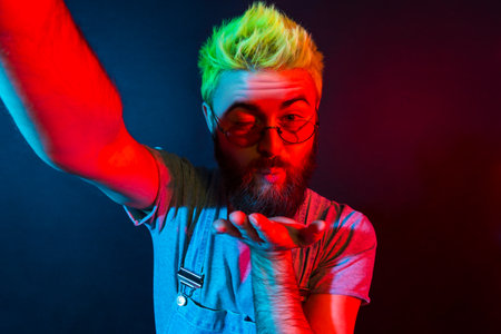 Romantic bearded hipster man with beard in denim overalls talking via web camera with girlfriend,...