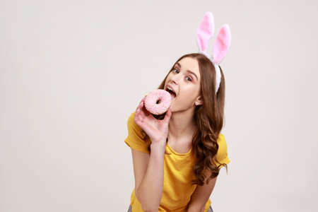 Happy playful teenager girl with brown hair in yellow casual T-shirt with pink bunny ears, biting...