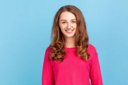 Portrait of smiling woman with wavy hair wearing pink pullover expressing positive emotions and...