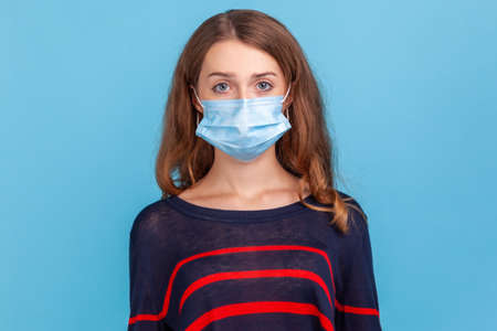 Serious woman wearing striped casual style sweater and medical mask prevent infection, airborne...