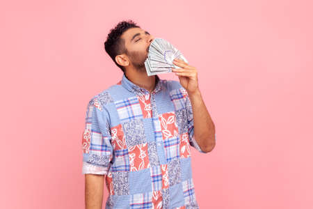 Portrait of handsome greedy arrogant man with beard smelling dollar banknotes with expression of...