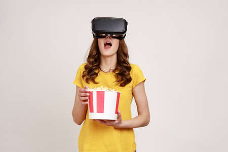 Young girl in yellow T-shirt getting experience VR headset, using augmented reality eyeglasses being...