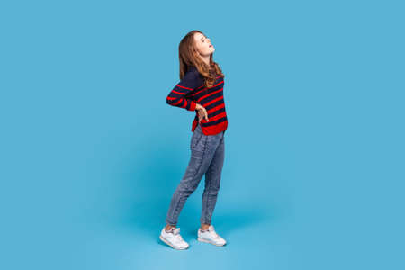 Full length of woman wearing striped casual style sweater, having strong backache, touching and...