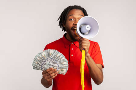Portrait of man with dreadlocks wearing red casual style T-shirt, screaming in megaphone holding fan...