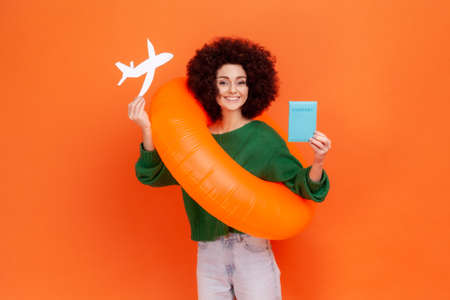 Satisfied positive woman with Afro hairstyle wearing green casual style sweater holding orange...