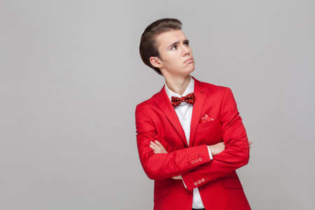 Need to think. Portrait of confused thoughtful gentleman in red tuxedo and bow tie crossing hands and looking up with doubtful face, pondering idea. indoor studio shot isolated on gray backgroundの写真素材