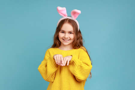 Portrait of little girl stands with pink bunny ears, child having fun playing game, looks at camera,...
