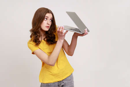 Woman with curly hair in urban style yellow T-shirt peeking out half-closed laptop with sly...
