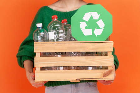 Anonymous woman wearing green casual style sweater holding box with plastic bottles ans green...