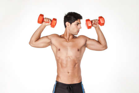 Portrait of shirtless sexy sportsman looking away, standing with raised arms, holding dumbbells, having workout for biceps and triceps. Indoor studio shot isolated on white background.の写真素材