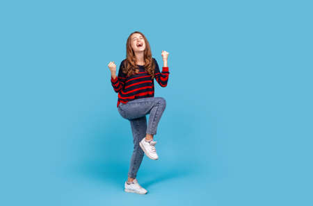 Full length positive satisfied woman wearing striped casual style sweater and jeans, raised clenched...
