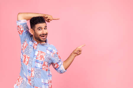 Wow, attention to advertising. Portrait of happy bearded man pointing to side copy space with both hands and showing blank wall for idea presentation. Indoor studio shot isolated on pink background.の写真素材
