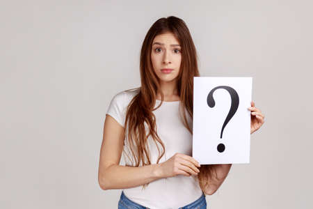 Portrait of confused thoughtful woman looking at camera, holding paper with question mark, thinks...