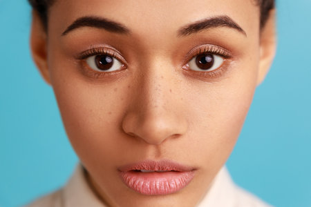 Close up portrait of beautiful serious woman model with natural makeup, looking at camera with calm concentrated facial expression. Indoor studio shot isolated on blue background.の写真素材