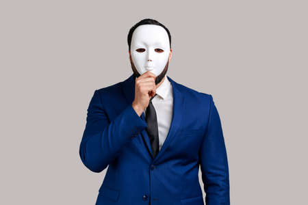 Anonymous unknown businessman covering her face with white mask, hiding her real personality, anonymity, wearing official style suit. Indoor studio shot isolated on gray background.の写真素材