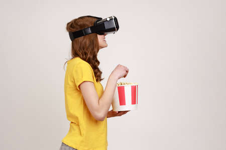 Profile portrait of young brown haired woman in VR headset watching movie with popcorn, wearing...