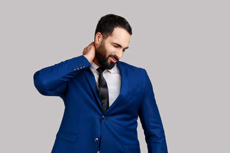 Bearded businessman touching neck feeling pain and numbness, worried about muscle tension,...