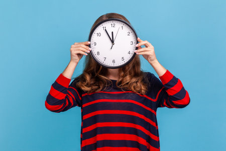 Portrait of unknown anonymous woman wearing striped casual style sweater, hiding her face, time...