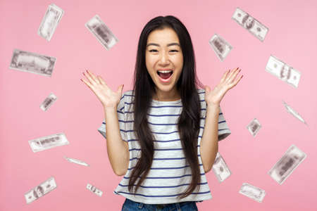 Oh my god, wow. Portrait of amazed young woman looking at camera with big eyes, absolutely shocked of money rain falling from up. indoor isolated on pink backgroundの写真素材