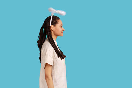 Side view portrait of smiling woman with black dreadlocks with nimbus over her head, looking ahead with toothy smile, expressing positive emotions. Indoor studio shot isolated on blue background.の写真素材