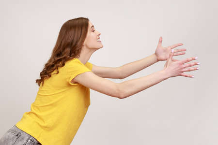Side view of kind young female with brown hair outstretching hands as if giving for free, offering...