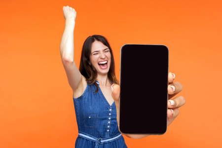 Portrait of happy joyful girl screaming with happiness showing mobile advertisement mockup area and celebrating her victory. indoor studio shot isolated on pink backgroundの写真素材