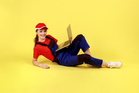 Full length portrait of worker woman lying on floor smiling at camera, holding laptop for online...
