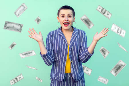 Oh my god, wow. Portrait of amazed young woman looking at camera with big eyes, absolutely shocked of money rain falling from up. indoor isolated on green backgroundの写真素材