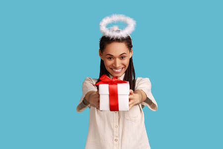 Portrait of cheerful woman with black dreadlocks and halo overhead holding gift box, charity...