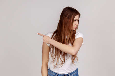 Portrait of resentful upset attractive woman turning away with disgust and ordering to leave, showing way out, feeling betrayed, wearing white T-shirt. Indoor studio shot isolated on gray background.の写真素材