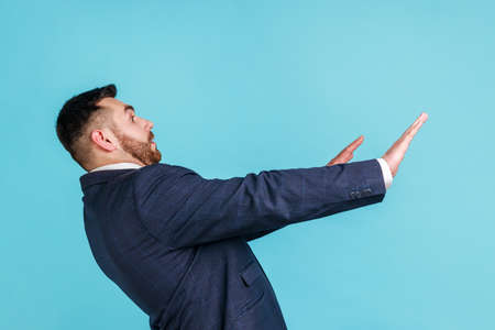 No, its scary. Profile portrait of frightened shocked man in suit raising hands in fear, looking horrified and panicking, hiding from phobia. Indoor studio shot isolated on blue background.の写真素材