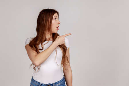 Portrait of surprised shocked woman pointing empty space, showing blank wall for commercial idea,...