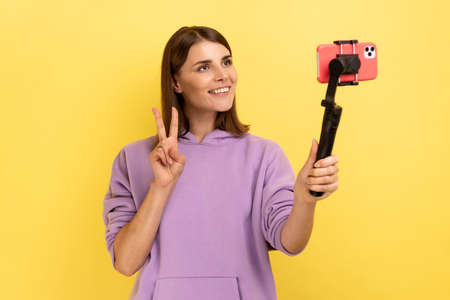 Portrait of happy positive woman with phone on stabilizer, broadcasting livestream, looking at...