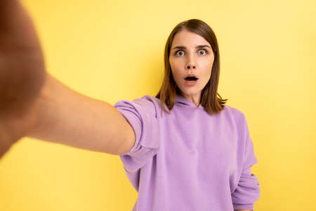Portrait of surprised woman taking selfie with shocked facial expression, looking with big eyes and...