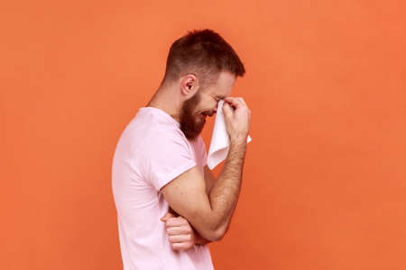 Portrait of sad alone hopeless bearded man standing, holding his head down and crying, wipes tears...