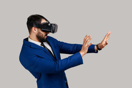 Side view of bearded man in vr glasses, stretching hands forward, trying to grab something while...