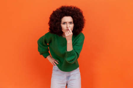 Woman with Afro hairstyle looking with incredulous suspicious gaze and touching nose, gesturing you...