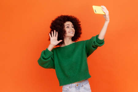 Adorable blogger woman with Afro hairstyle wearing green casual style sweater waving hand to...