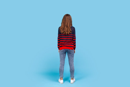 Full length back portrait of woman woman wearing striped casual style sweater, standing calm looking...