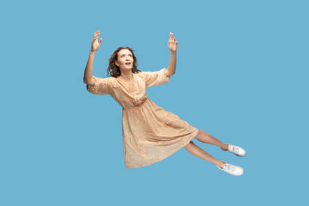 Hovering in air. Full length beautiful pensive girl in yellow dress levitating flying in mid-air,...