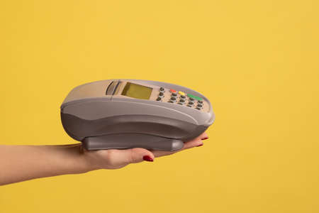 Profile side view closeup of woman hand holding POS or terminal payment or pay pass device. Indoor...