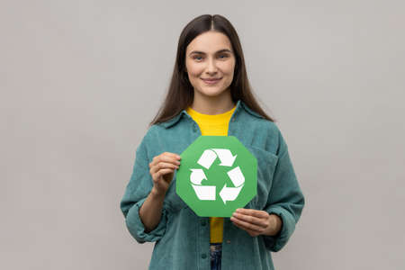 Smiling woman with dark hair holding in hands green recycling sing, ecology concept, looking at...